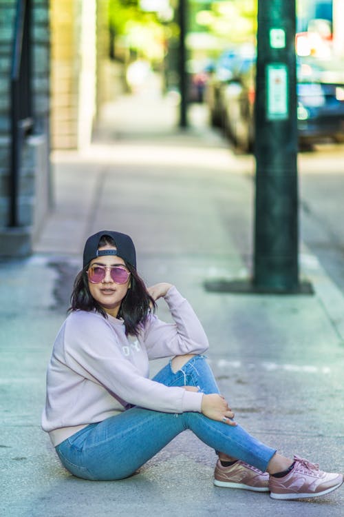 A woman sitting on the sidewalk wearing a hat and jeans