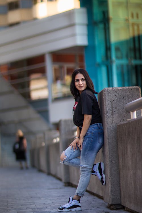 Free A woman leaning against a wall wearing jeans and a t - shirt Stock Photo