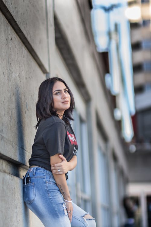 Free A woman leaning against a wall wearing jeans and a t - shirt Stock Photo