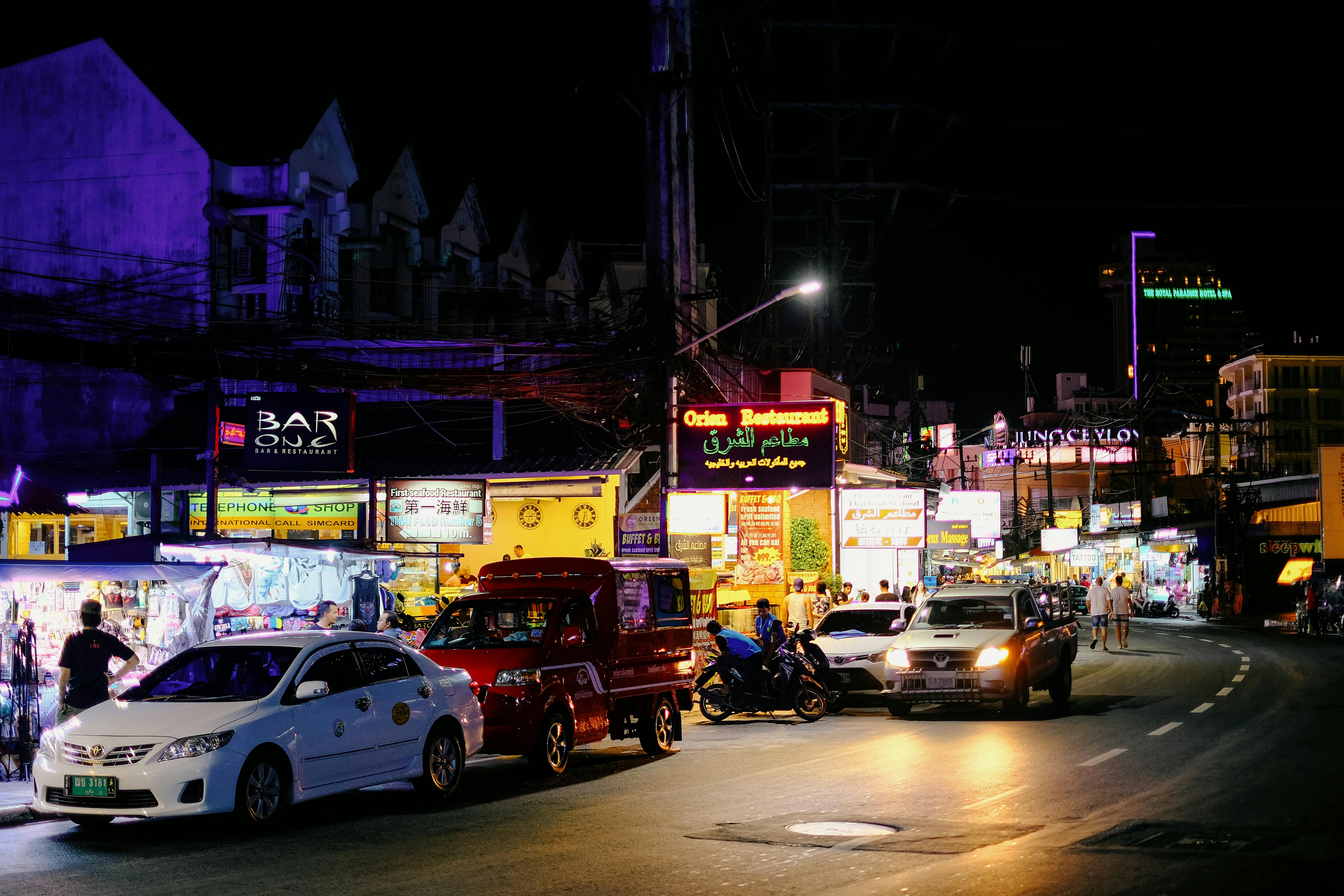 Scène nocturne animée dans une rue animée de Bangkok, éclair ée par des enseignes au néon et bondée de circulation.