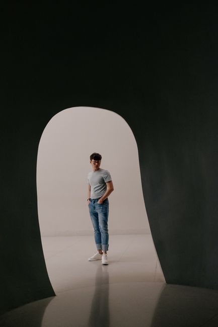 Young man in casual attire stands in a modern gallery in Bangkok.