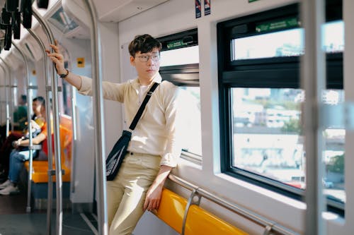 Young Man in a Beige Shirt and Pants Traveling by City Train