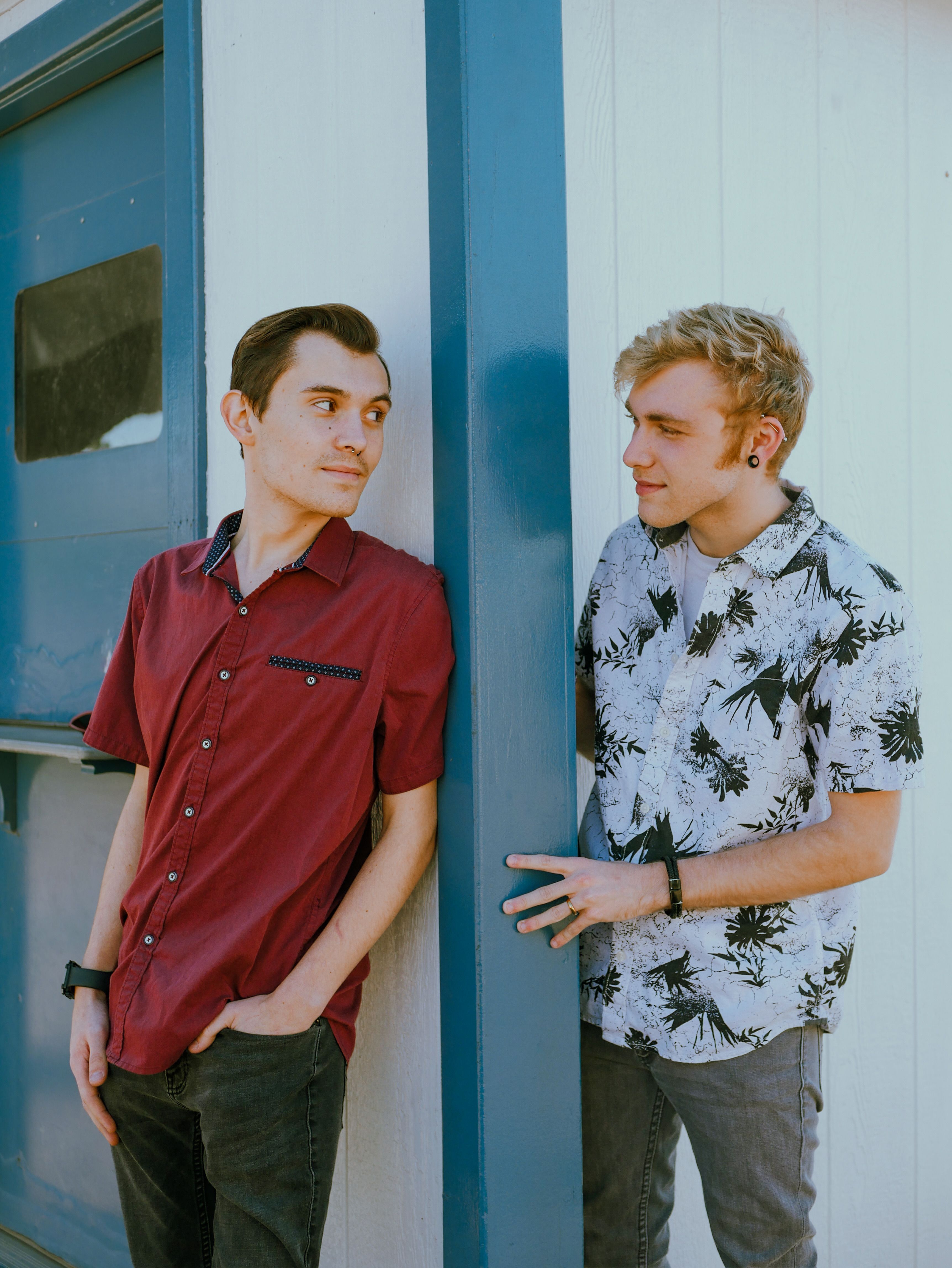 Two young men in casual shirts standing against a blue wall, enjoying a conversation.