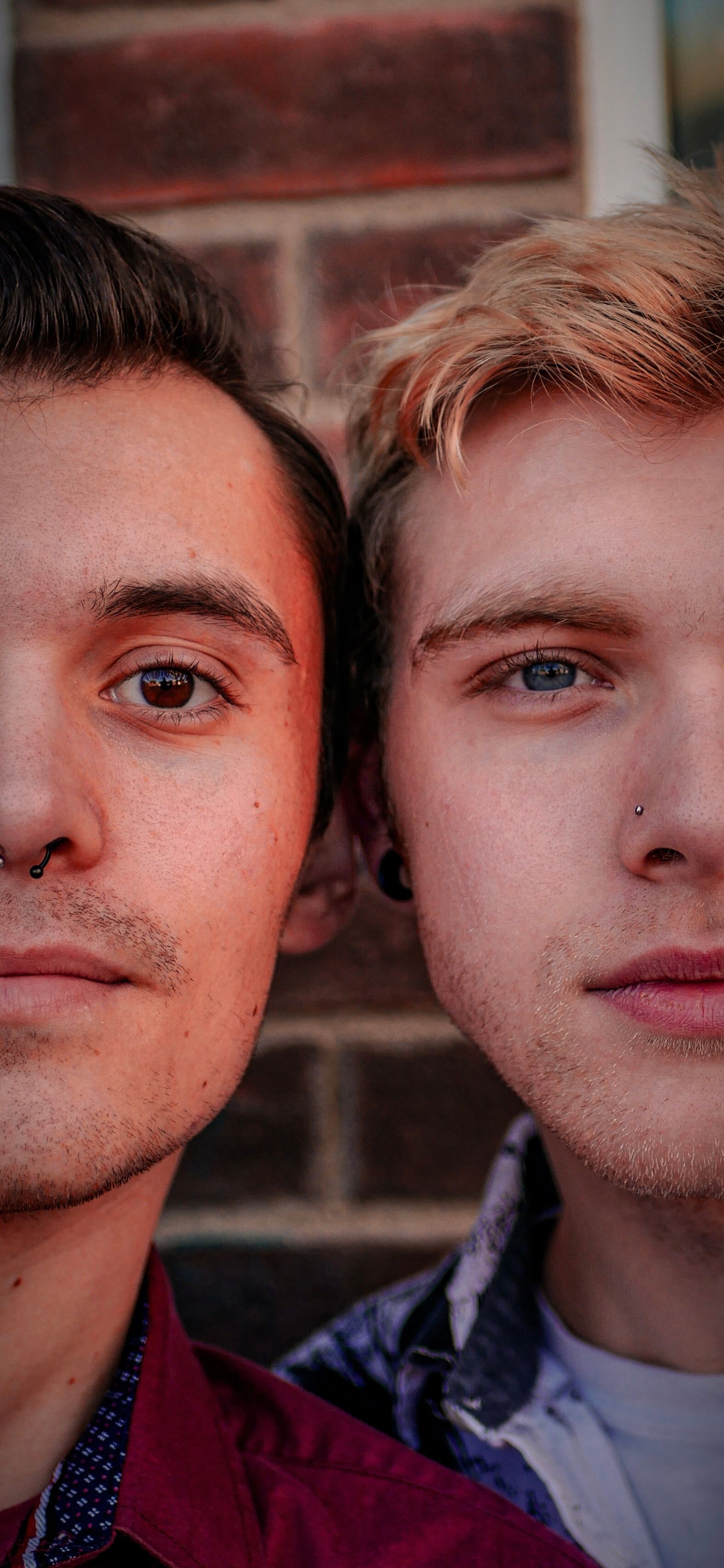 Engaging close-up portrait of two young men standing outdoors against a brick background in casual attire.