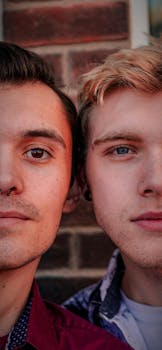 Engaging close-up portrait of two young men standing outdoors against a brick background in casual attire.