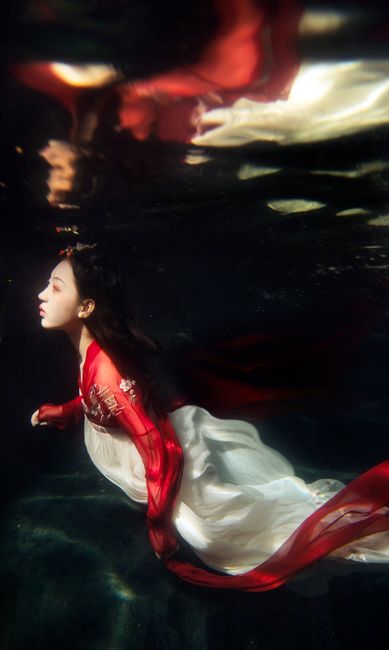 A woman elegantly swimming underwater wearing traditional red and white Hanfu, exhibiting cultural and artistic beauty.