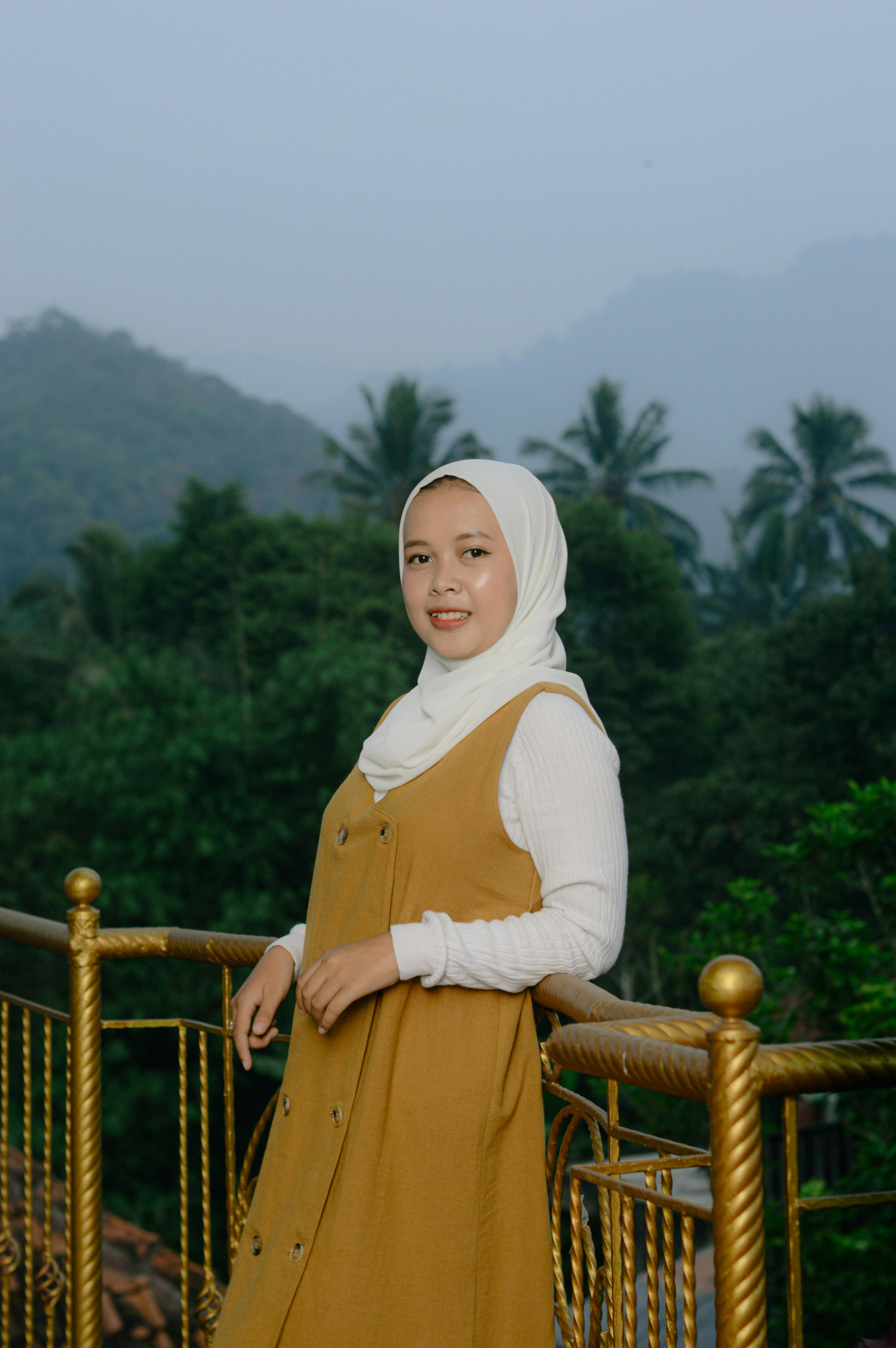 Asian woman smiling on a balcony with lush green mountains and palm trees in the background.