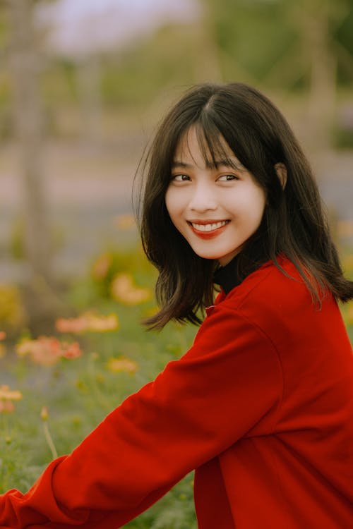 Young Woman in a Red Blouse Sitting Outside and Smiling 
