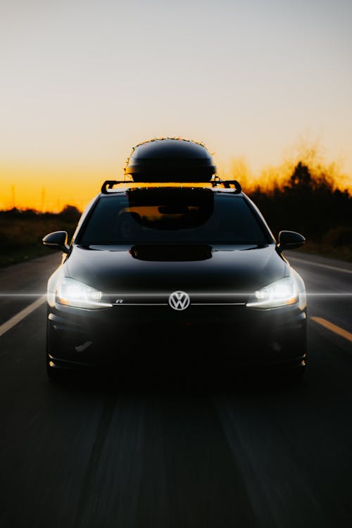Black Volkswagen Golf with a Roof Box Speeding Down the Road at Dusk