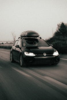 A sleek Volkswagen Golf speeding down a rural road with a rooftop cargo box, captured in a dramatic shot.