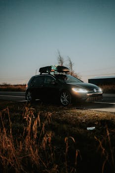 A modern car with rooftop cargo parked on a country road at dusk, ideal for travel themes.