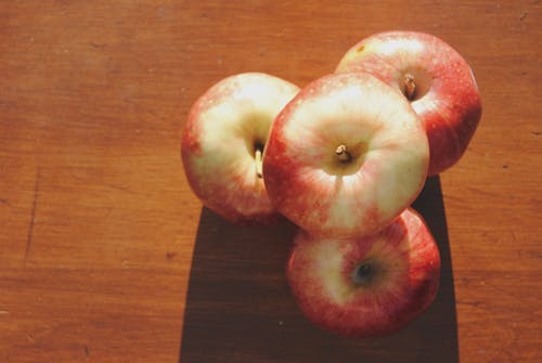 Top view composition of sweet red apples arranged together on shabby wooden table under bright sunlight