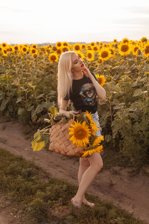 Blonde Woman Standing with Sunflowers on Field