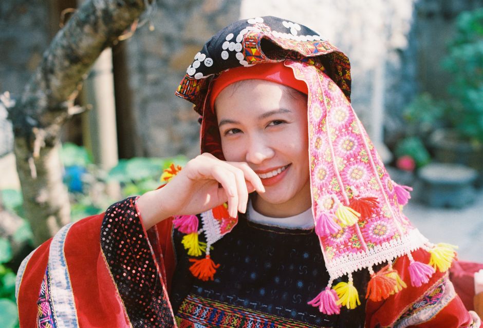 A vibrant portrait of a smiling woman wearing colorful traditional clothing and a decorative hat outdoors.