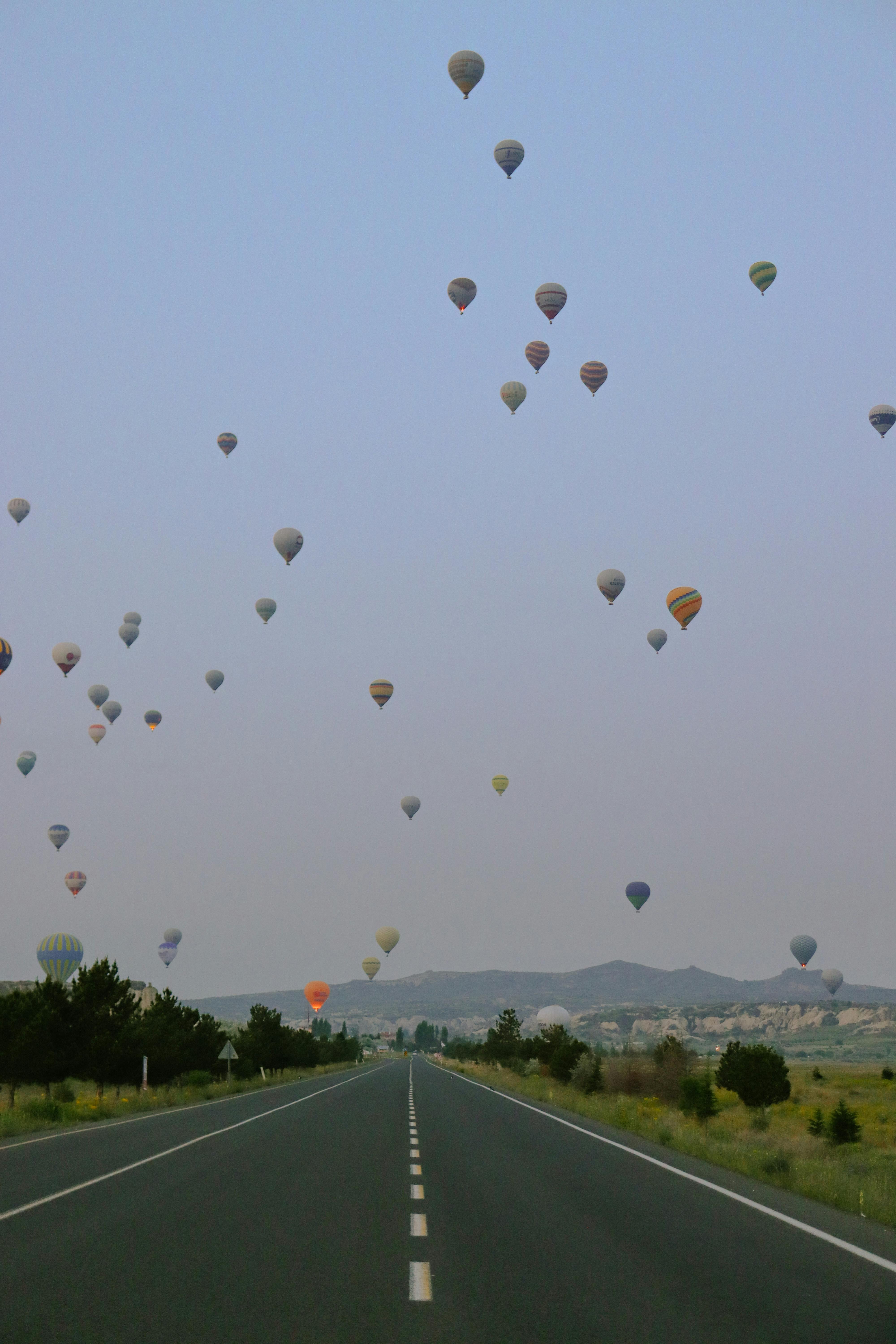 Hot air balloons fill the sky over a scenic highway in Türkiye, offering a serene view.