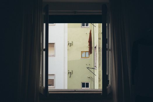 A view of an urban apartment building facade framed by an open window.