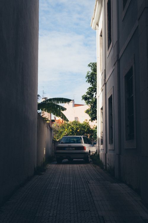 Free A narrow urban alley with a parked car, flanked by tall buildings, under a clear sky. Stock Photo