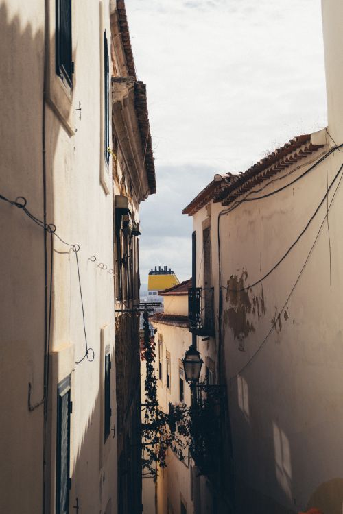Free Sunlit narrow alleyway with historic European architecture and vintage lanterns, perfect for travel exploration. Stock Photo