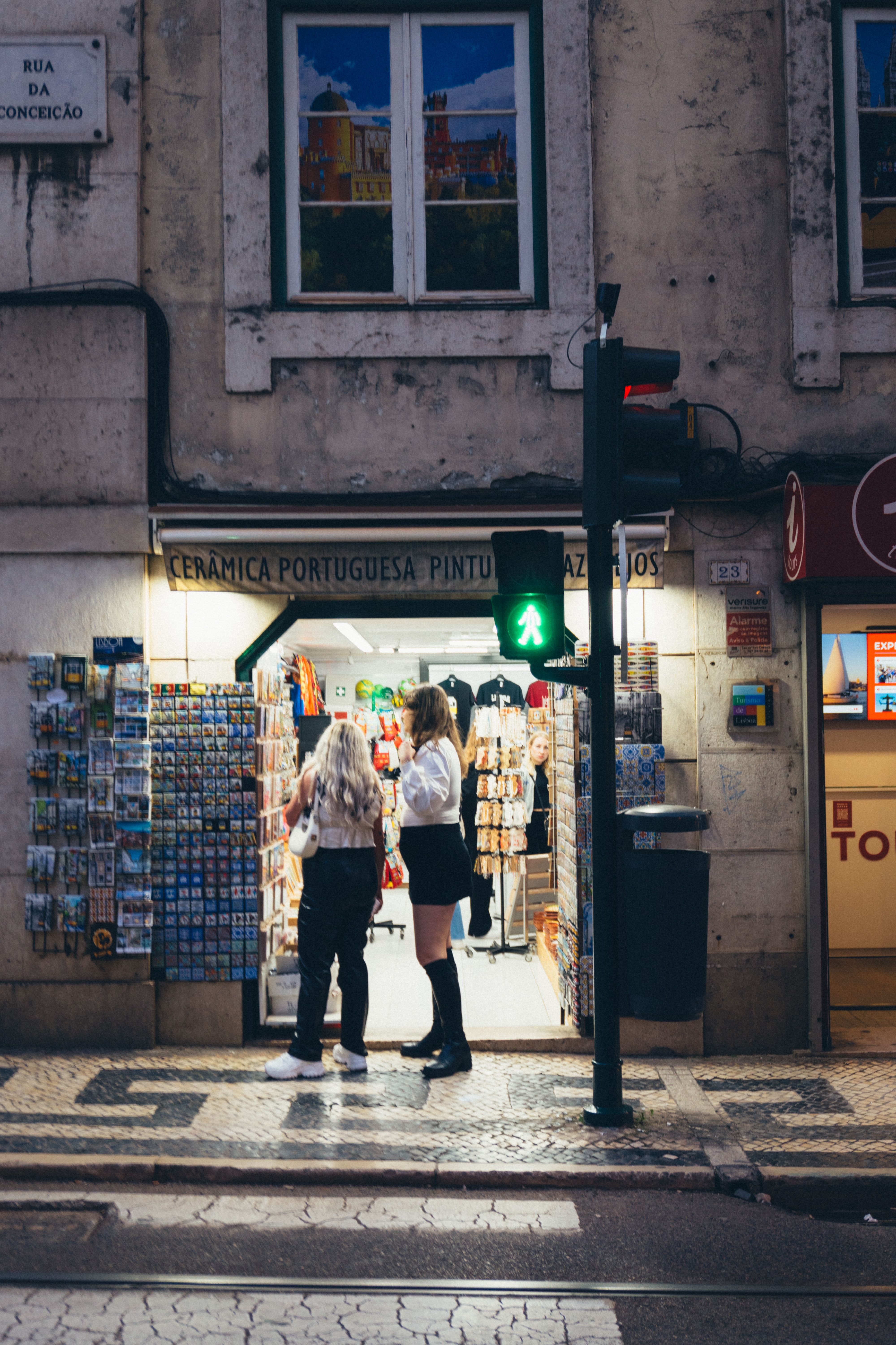 Two women shopping at a well-lit Lisbon store entrance in the evening.