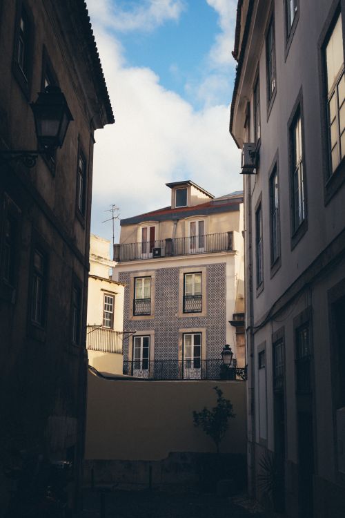 Free A narrow alleyway in Lisbon showcasing classic Portuguese architecture under a blue sky. Stock Photo