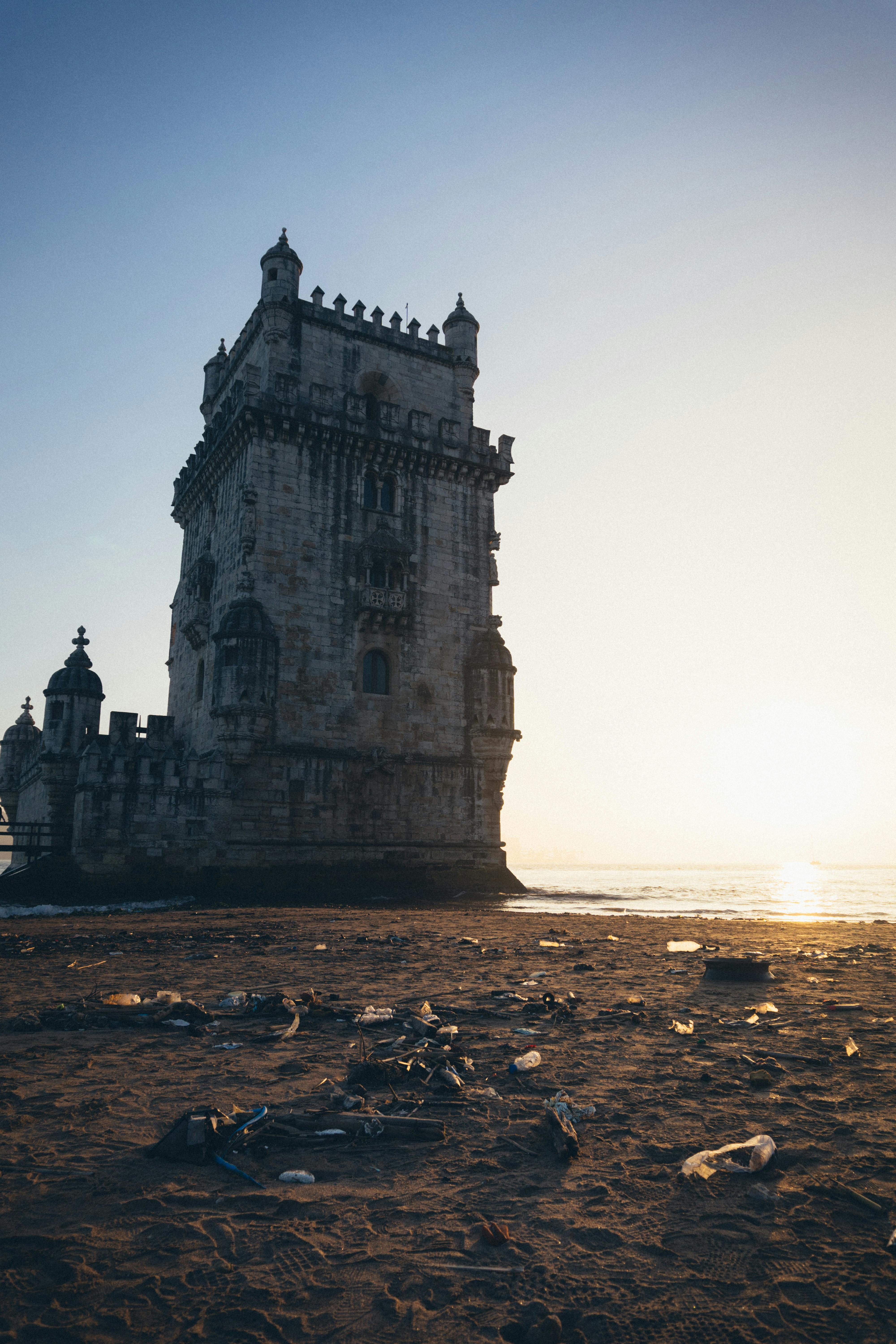 Belem Tower stands on a sandy Lisbon beach at sunrise, with a serene clear sky.