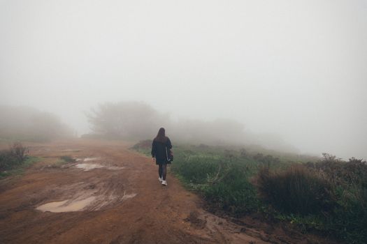 Scenic view of a woman walking on a foggy, dirt path surrounded by mist and natural landscape.