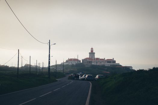 Cabo da Roca lighthouse stands in foggy dusk over a scenic Portuguese road.