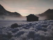 冬日薄雾笼罩的山间，一座木屋静立于白雪皑皑的宁静景象中