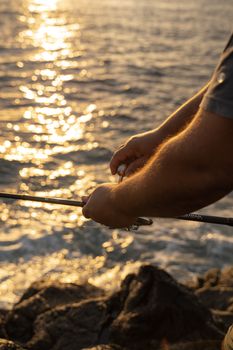 Close-up of a man fishing by the sea during sunset with beautiful reflections.