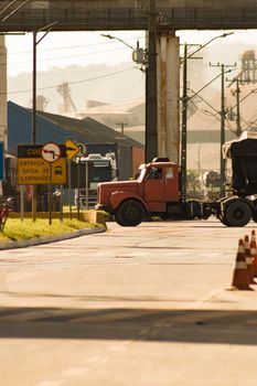 Trucks maneuvering on a city street under bright daylight near industrial structures.