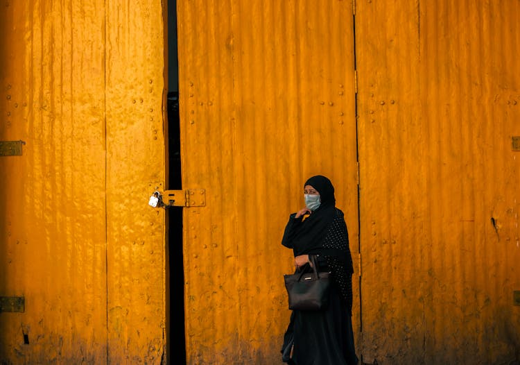 Woman In Headscarf And Face Mask By Closed Door Of Warehouse