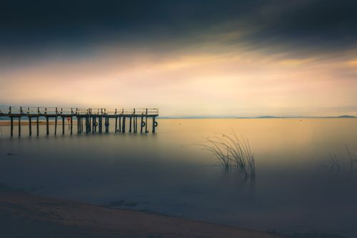 Free Tranquil sunset view of a wooden pier on a calm lake at Barra do Ribeiro, RS, Brazil. Stock Photo