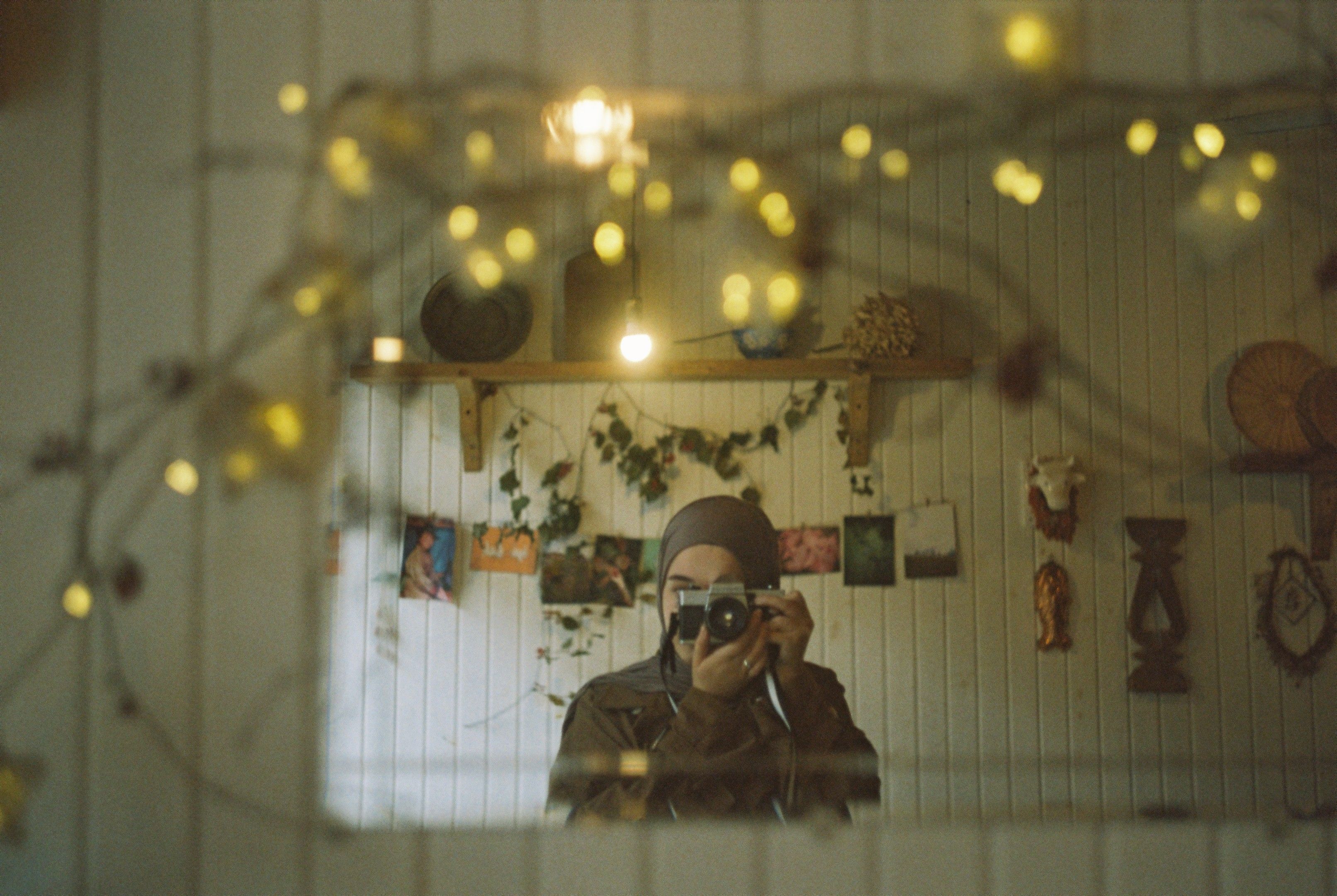 A woman takes a self-portrait in a mirror surrounded by warm lights.