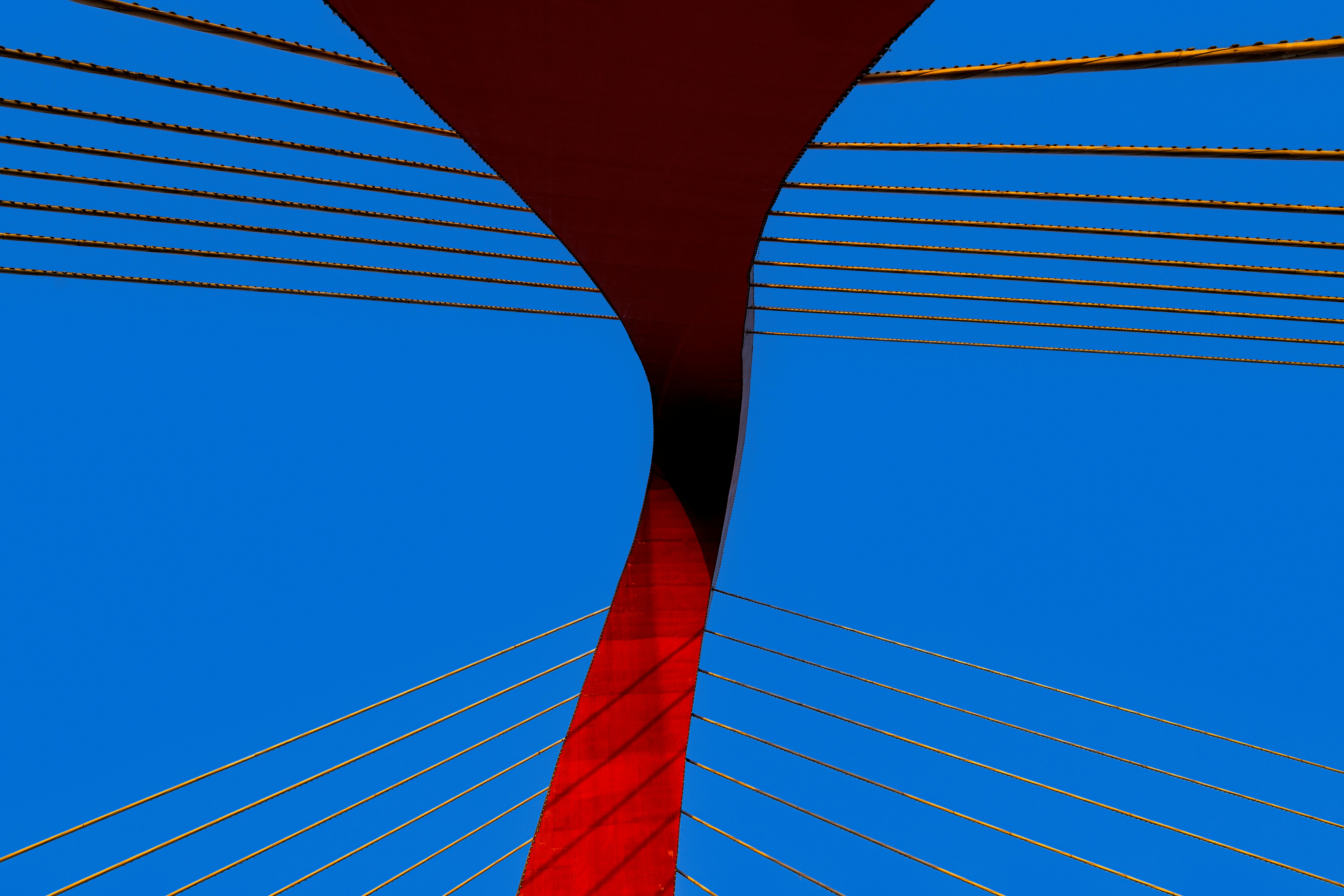 A striking modern bridge with red and blue colors and abstract lines against a clear sky.