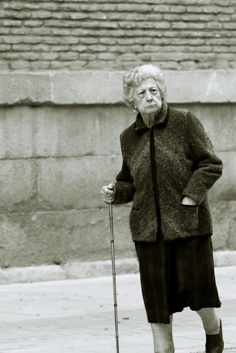 Elderly Woman Walking On The Sidewalk With A Cane