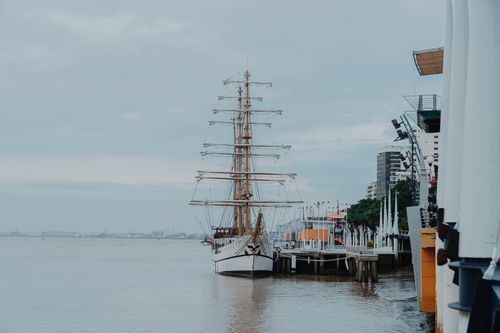 Free A majestic tall ship moored at a city pier, offering a serene urban waterfront view. Stock Photo