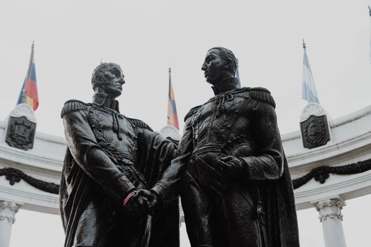 Historic statues at Hemicycle de la Rotonda, Guayaquil, Ecuador, captured with flags in the background.