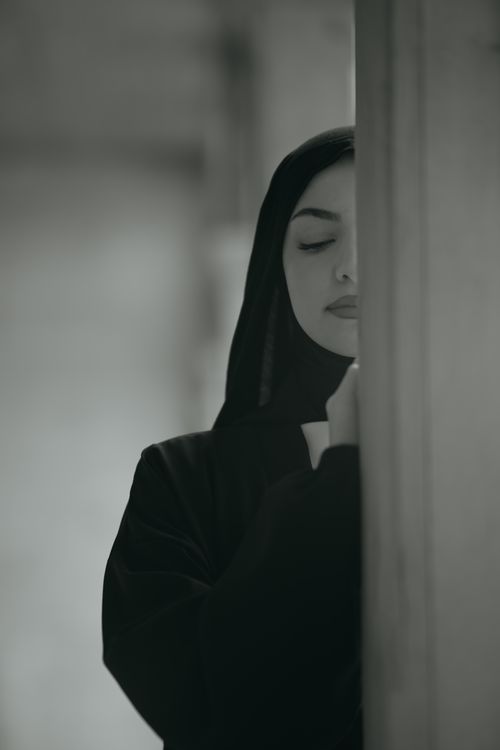 Free A woman in a black abaya and hijab leans against a wall, eyes closed, in a serene moment. Stock Photo