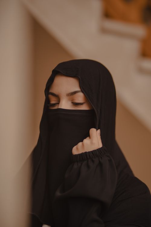 Free Emotive portrait of a woman wearing a traditional black hijab and niqab indoors. Stock Photo