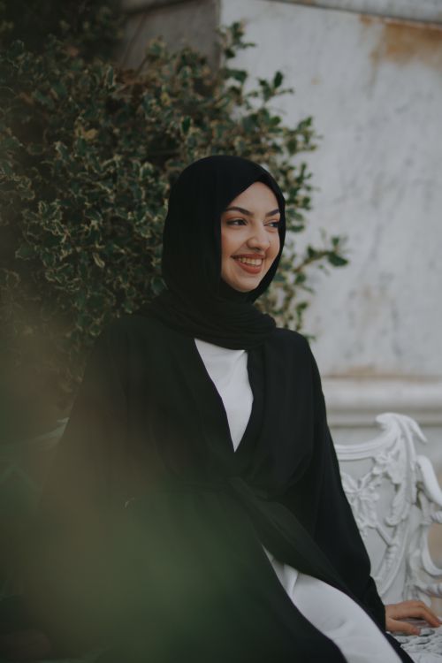 Free Young woman wearing a black hijab, sitting outdoors and smiling. Stock Photo