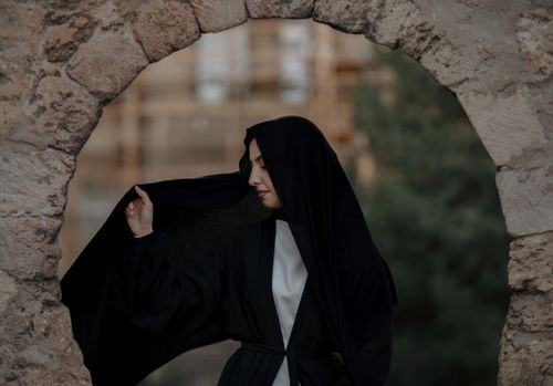Free Young woman in a traditional black hijab poses outdoors in a stone archway. Stock Photo