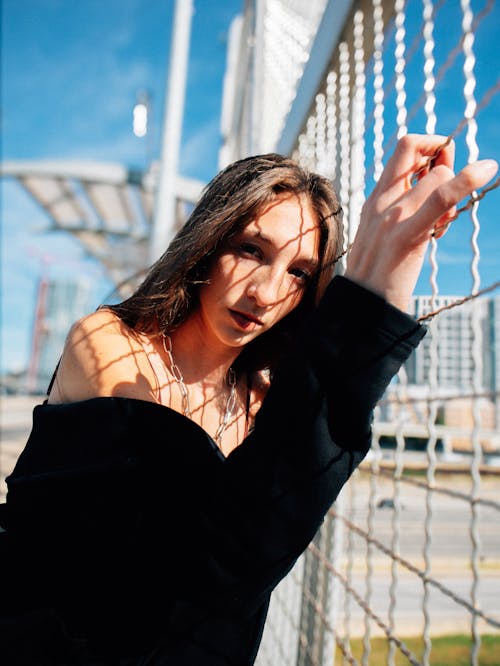 A woman leaning against a fence with her hand on her chin