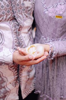 Close-up of a bride and groom holding a gold bracelet during their wedding ceremony, emphasizing love and unity. - Fotografer Sidoarjo