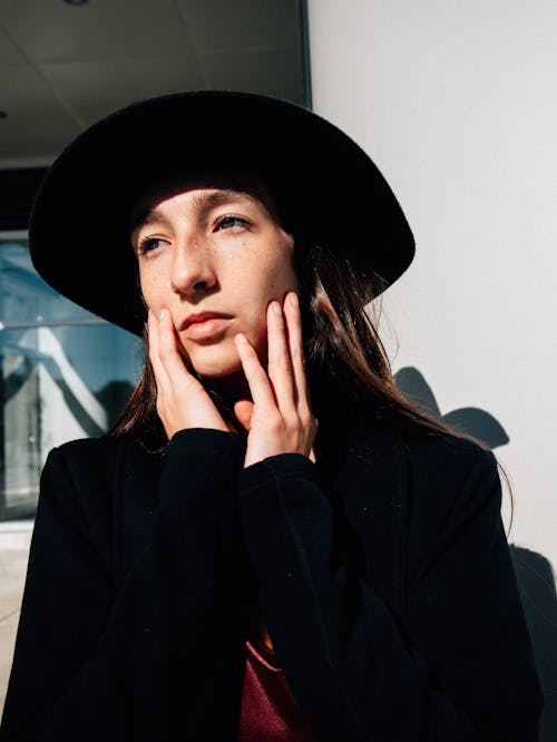 woman wearing a black coat and hat posing with hand on her face 