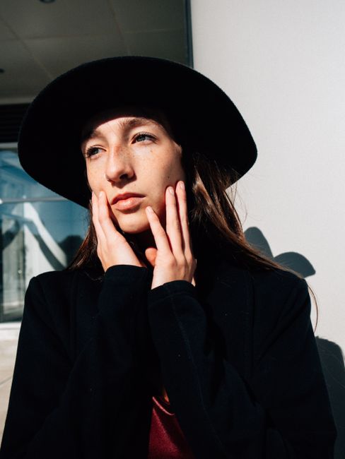 Woman posing outdoors in a black hat with cinematic lighting and thoughtful expression.