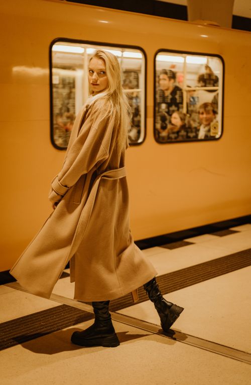 Free A fashionable young woman in a coat standing on a subway platform, looking back stylishly. Stock Photo