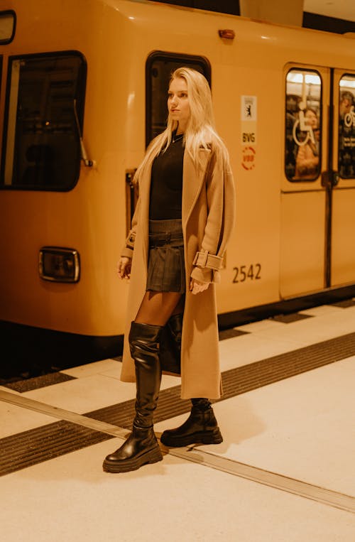 Young Woman in a Coat and Boots Standing on a Subway Platform 