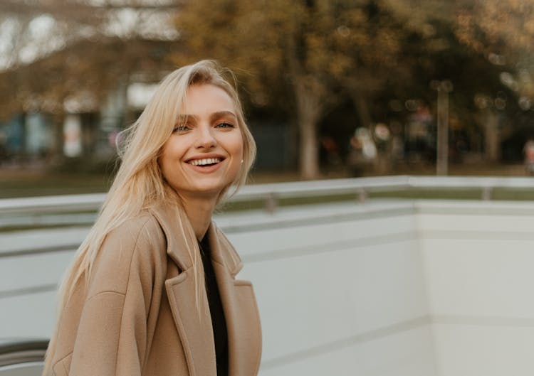 Young Woman In A Coat Smiling And Standing Outside In City 