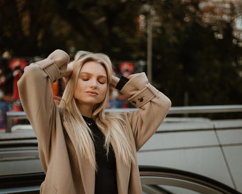 Young Woman in a Coat Standing Outside with Eyes Closed and Hands in Hair 