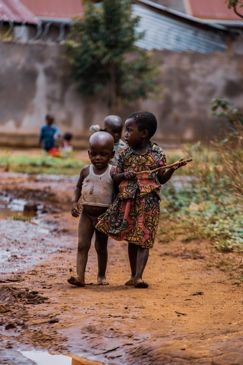 Free Young children walking playfully on a muddy path in a rural village setting. Stock Photo